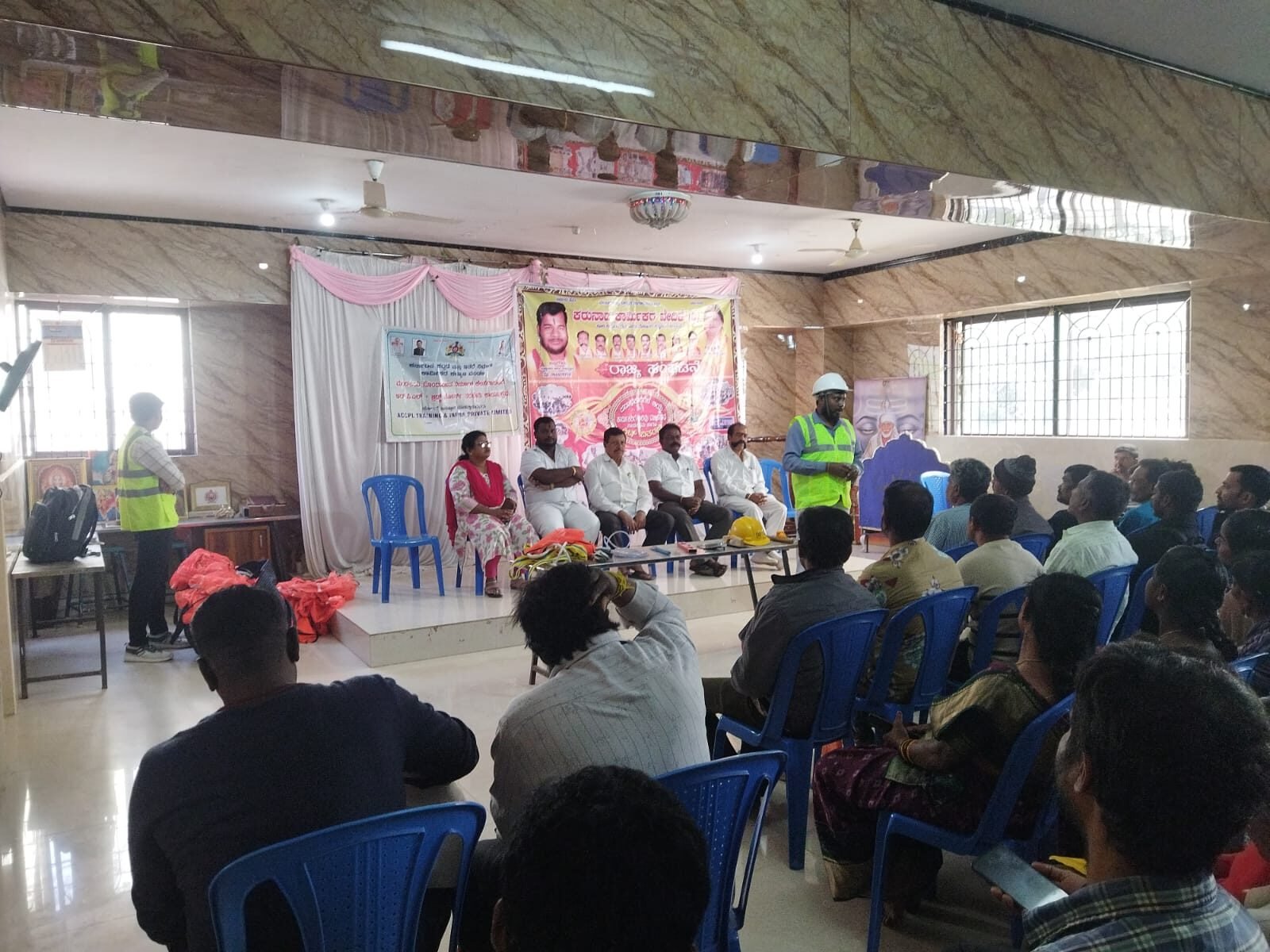 Trainer speaking to a large group of workers seated in a hall during the program