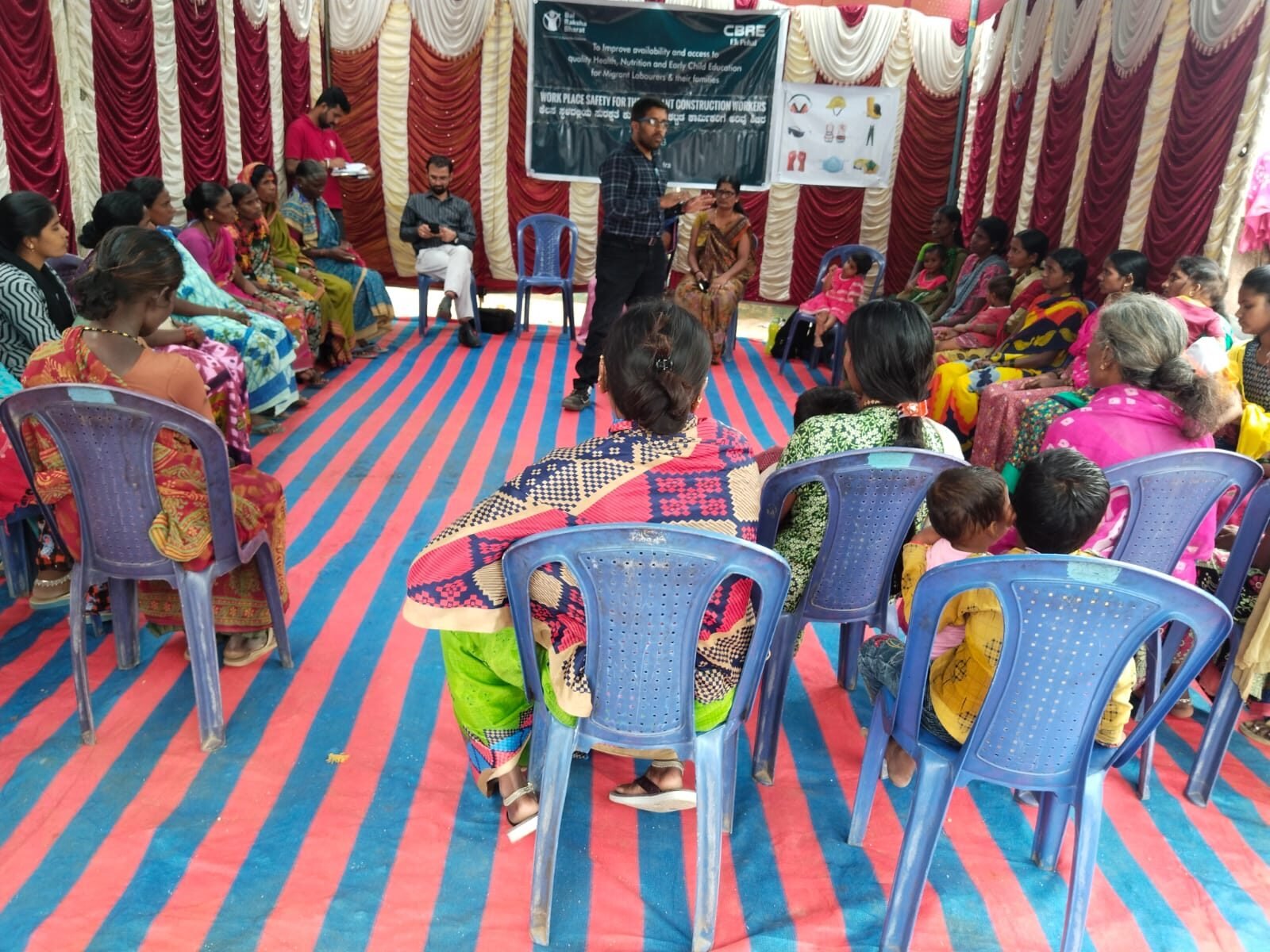 Facilitator addressing a large group of women and children under a tent during an awareness session